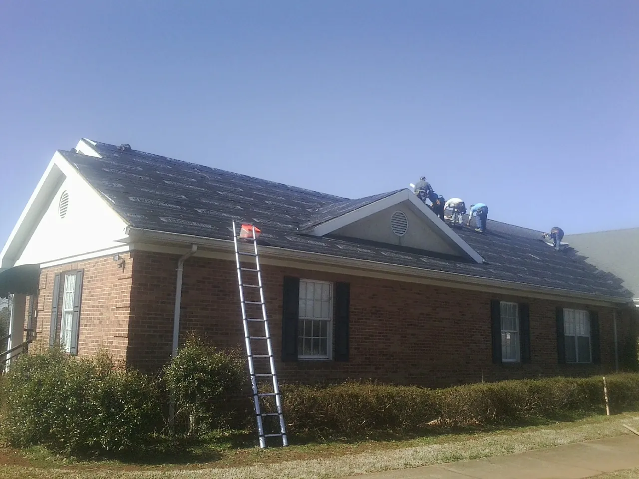 Crew tearing shingles off a brick ranch roof with a ladder set — Emergency Roof Repair work by our crew in Kellogg