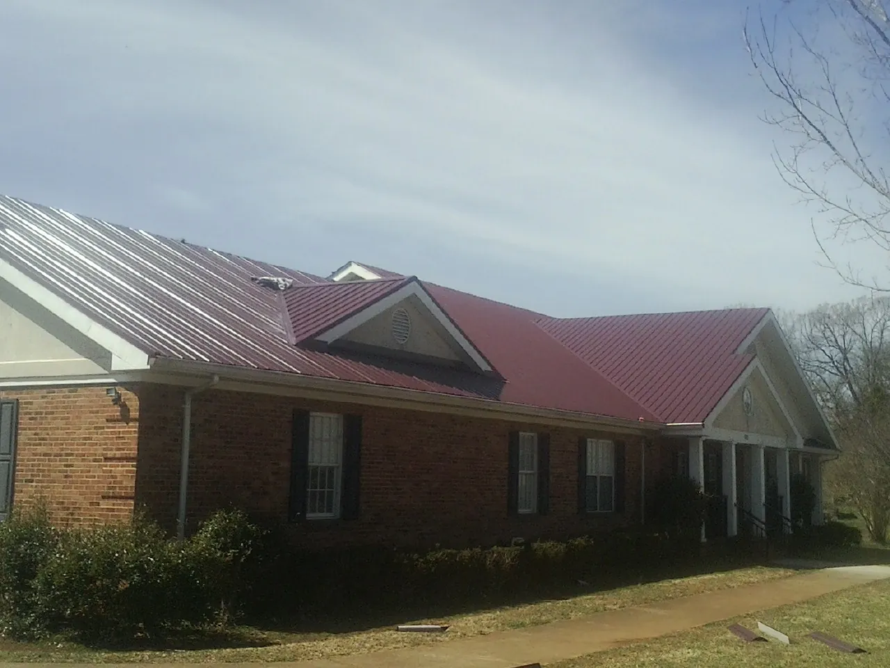 Red metal roof with gabled entries on a long brick building, from a Hail Damage Roof Repair job in Kellogg