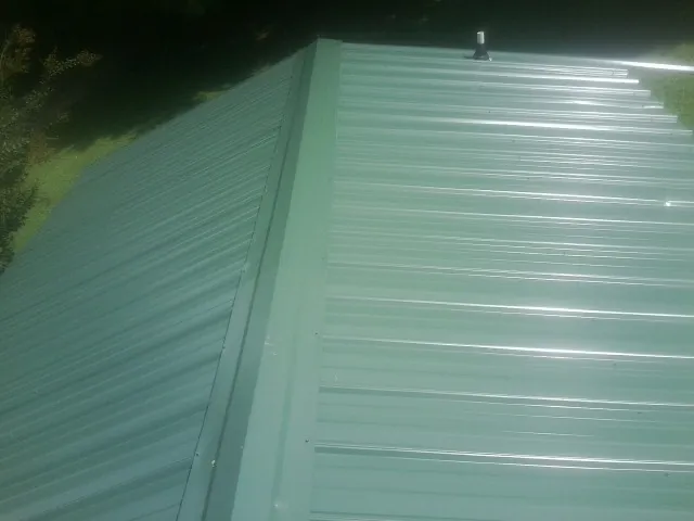 New green metal panels meeting at the ridge of a roof — Flat Roof Repair work by our crew in Kellogg