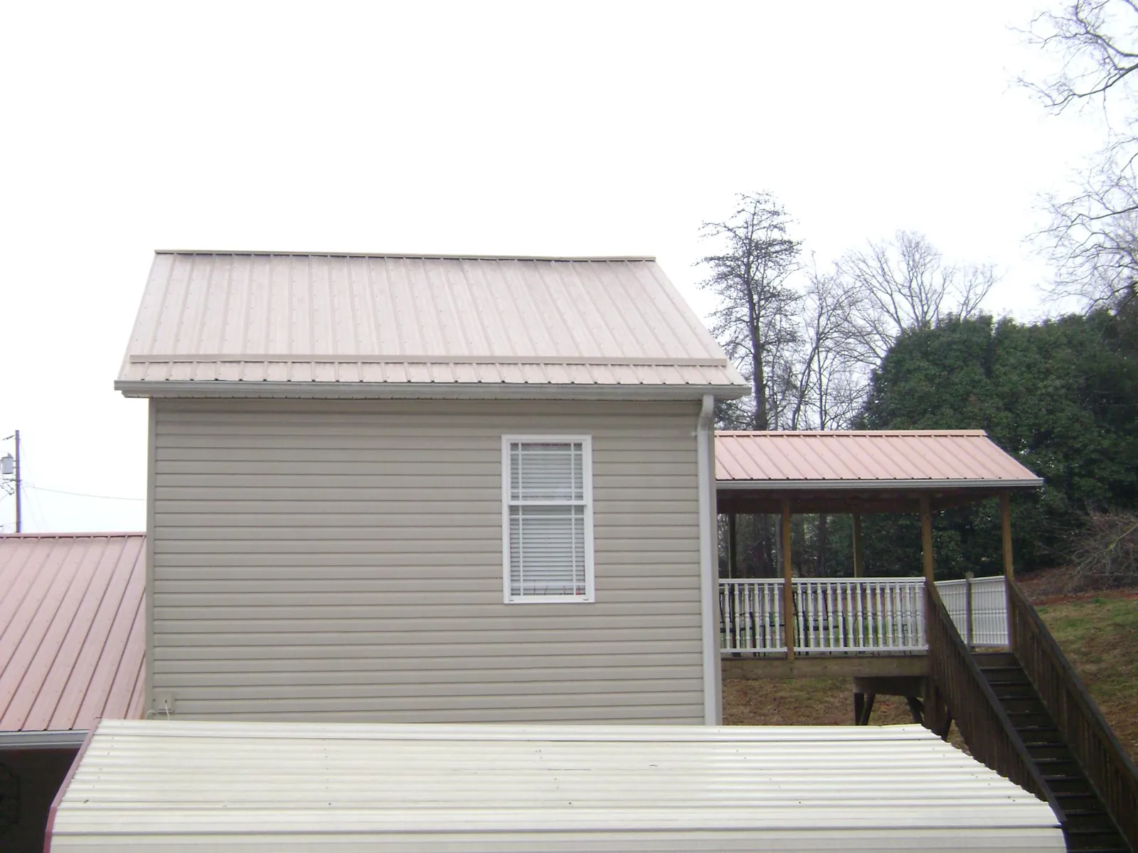 Tan metal roofs on a two story addition and attached porch, from a Roof Replacement job in Kellogg